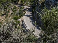 a motorcycle is driving down the middle of a mountain pass surrounded by trees and hills