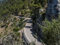 a motorcycle is driving down the middle of a mountain pass surrounded by trees and hills