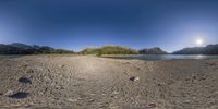 a panoramic image of the mountains, river and sky by a sandy shore