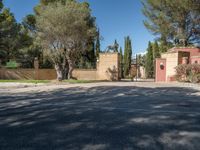 an empty parking lot in front of a tree covered house with a gate and gate to a yard