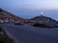 a highway near a cliff with a small church on it at sunset by the ocean