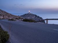 a highway near a cliff with a small church on it at sunset by the ocean