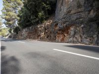 a person riding down the road by some cliffs and trees with no one on it