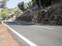 a person riding down the road by some cliffs and trees with no one on it