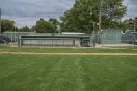 there is a baseball field with several dug outs behind the baseball field in which there is a bench, green grass, and the stadium has a sky