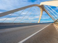 a large metal bridge spanning a highway under a cloudy blue sky on the side of the road