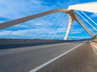 a large metal bridge spanning a highway under a cloudy blue sky on the side of the road