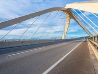 a large metal bridge spanning a highway under a cloudy blue sky on the side of the road