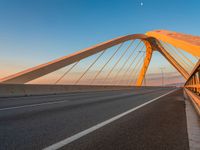 a road with yellow lights going over it that goes into the distance at sunset with a long bridge stretching over it