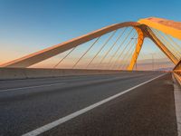 a road with yellow lights going over it that goes into the distance at sunset with a long bridge stretching over it