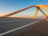 a road with yellow lights going over it that goes into the distance at sunset with a long bridge stretching over it