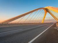 a road with yellow lights going over it that goes into the distance at sunset with a long bridge stretching over it