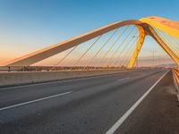 a road with yellow lights going over it that goes into the distance at sunset with a long bridge stretching over it