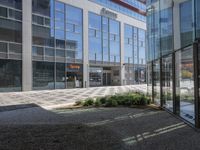 an open courtyard with a sidewalk and building in the background, and a small sign in between two tall glass buildings