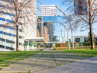 a walkway that runs through a grassy field area between tall buildings and grassy lawn with several bushes in the foreground