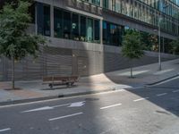 the empty bench is in front of the office building on the sidewalk in the city