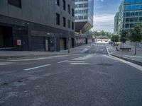 the empty street has white lines in it's paint on asphalt and buildings in the background