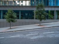 the sidewalk is next to a tall office building in the cityscape, with two trees and a motorcycle