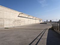 a man in black shirt doing a trick on skateboard on ramp area above cement wall with blue sky behind him