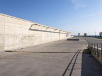 a man in black shirt doing a trick on skateboard on ramp area above cement wall with blue sky behind him