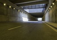 a paved road passes under a bridge with lights going down it into the distance under which is an illuminated wall and overhang