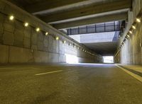 a paved road passes under a bridge with lights going down it into the distance under which is an illuminated wall and overhang