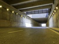 a paved road passes under a bridge with lights going down it into the distance under which is an illuminated wall and overhang