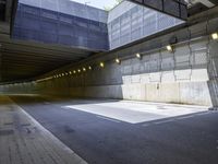 an empty walkway with lights on each end in front of a building with dark walls