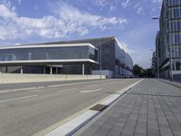 the street has two empty roads and two buildings with large windows on one side with a sky background