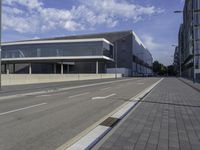 the street has two empty roads and two buildings with large windows on one side with a sky background