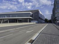 the street has two empty roads and two buildings with large windows on one side with a sky background