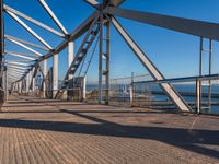 the walkway of a bridge over looking the water and boats docked in the distance on a bright, clear day