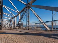 the walkway of a bridge over looking the water and boats docked in the distance on a bright, clear day