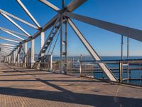 the walkway of a bridge over looking the water and boats docked in the distance on a bright, clear day