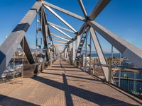 the walkway of a bridge over looking the water and boats docked in the distance on a bright, clear day