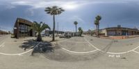 a view of a parking lot from a street with palm trees and buildings on one side