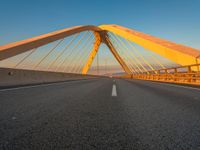 a large metal bridge with multiple cables extending out over a road, in the evening