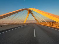 a large metal bridge with multiple cables extending out over a road, in the evening