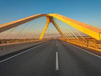 a large metal bridge with multiple cables extending out over a road, in the evening