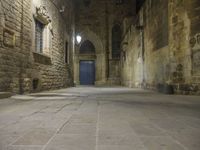 an old stone walkway in front of a doorway with blue door and brick walls leading into a room with tall windows