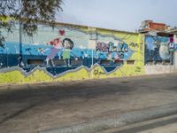 graffiti is painted on a street wall along a city street with a man riding a skateboard