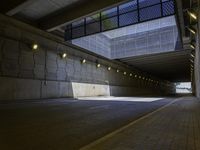 empty parking tunnel at an airport with brick walkway and low lighting on walkways, with skylights, stone walls, glass bale windows and metal grates