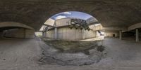 a panoramic view of the inside of a concrete structure with sand below and a blue sky above