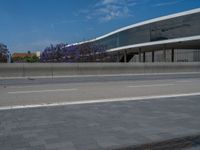 a man on a motorcycle passes by an empty parking lot under the freeway bridge that's across from the building