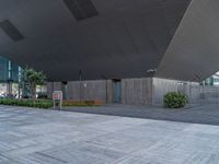 a building with grey roof in city area with multiple benches and tree trees in courtyard