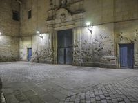 a stone walkway in front of an empty building at night with blue doorways and brick walling