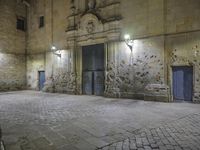 a stone walkway in front of an empty building at night with blue doorways and brick walling