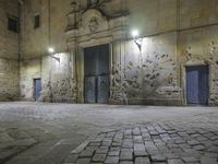 a stone walkway in front of an empty building at night with blue doorways and brick walling