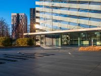 a building and its reflection in the glass on the pavement of a street with trees