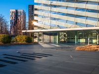 a building and its reflection in the glass on the pavement of a street with trees